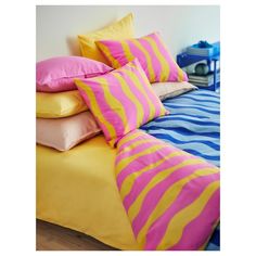 a bed topped with lots of pillows next to a blue and yellow comforter on top of a wooden floor