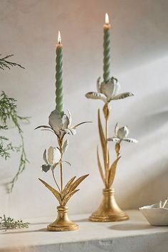 two candles are sitting next to each other on a table with flowers and leaves in it