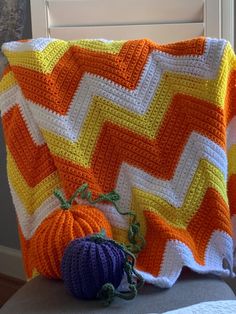 a crocheted blanket with two pumpkins sitting on the couch next to it