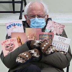 an elderly man wearing a face mask and holding several books in his hands while sitting on a chair