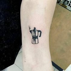 a black and white coffee pot tattoo on the left inner arm, with a cup in it