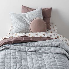 an unmade bed with two pillows and a pillow case on the headboard, in front of a white wall