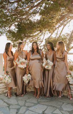 a group of women standing next to each other in front of a stone wall holding bouquets