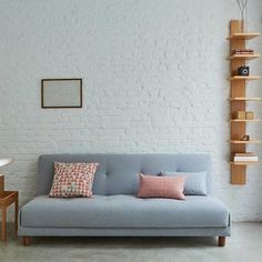 a blue couch sitting in front of a white brick wall next to a wooden table