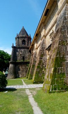 an old stone building with a clock tower in the background and grass on the ground