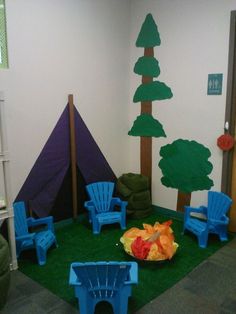 an indoor play area with blue chairs and green grass in front of the door, trees on the wall