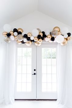 a white door with balloons hanging from it's side and black and gold decorations on the front