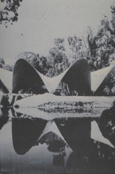 a black and white photo of a bridge over water with trees in the back ground