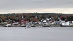 boats are floating on the water in front of a town with many trees and buildings