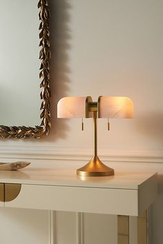 a table lamp sitting on top of a white desk next to a mirror and wall