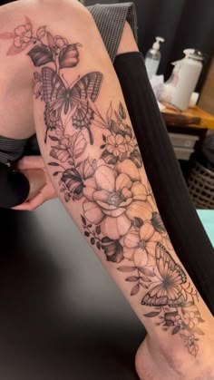 a woman's leg with flowers and butterflies tattoo on her left arm, sitting on a table