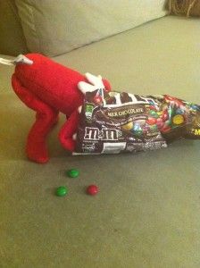 a red stuffed animal laying on top of a bed next to some candy bars and candies