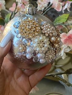 a hand holding a glass ornament with pearls and jewels on it, surrounded by flowers