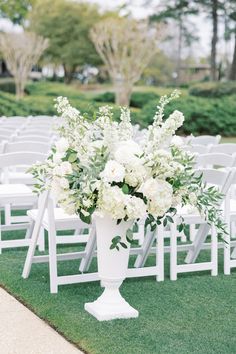 a white vase filled with flowers sitting on top of a grass covered field next to rows of chairs