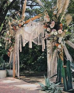 an outdoor wedding arch decorated with flowers and fringes, surrounded by succulent plants