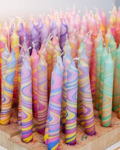 many colorful candles are lined up on a wooden stand in front of each other,