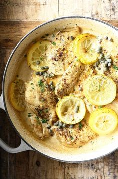 chicken with lemons and capers in a skillet on a wooden table top