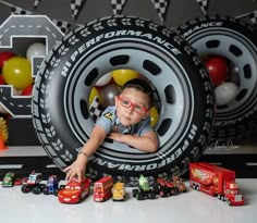 a young boy wearing red glasses sitting in front of a tire with cars on it