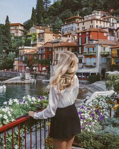 a woman standing on a balcony looking out at the water and houses in the background