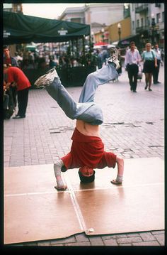 a young boy is doing a handstand on the sidewalk while people walk by