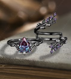 two rings with pink and blue stones on them sitting on top of a table next to a book