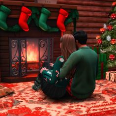 two people sitting on the floor in front of a christmas tree with stockings hanging over it