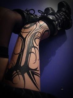 a person with tattoos on their legs and feet is sitting against a purple wall wearing black shoes