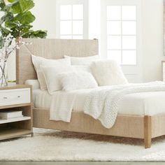 a bed with white linens and pillows in a room next to a plant on a table