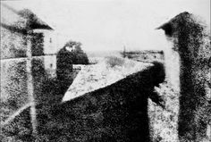 an old black and white photo of two people sitting on top of a roof looking out at the city