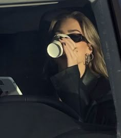 a woman drinking from a cup while sitting in a car