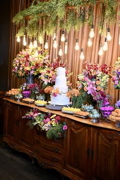 a wedding cake on a buffet table with flowers and greenery hanging from the ceiling