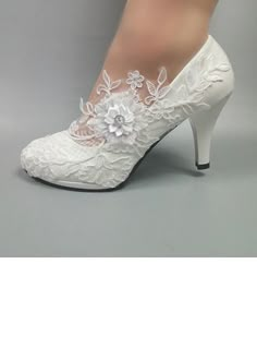 a woman's white wedding shoes with lace and flowers on the heel, against a gray background