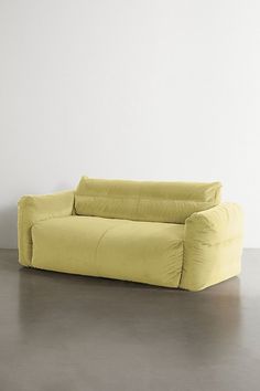 a yellow couch sitting on top of a cement floor next to a white wall in an empty room