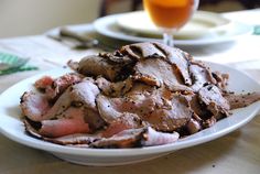 a white plate topped with sliced meat on top of a table next to a glass of orange juice