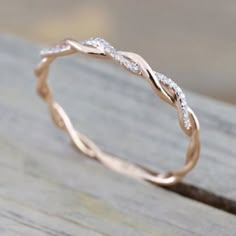 a rose gold wedding band with white diamonds on the inside and outside, sitting on top of a piece of wood