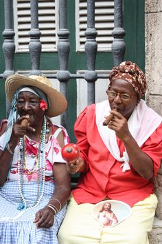 two women sitting next to each other on the steps eating food and drinking juice from their mouths