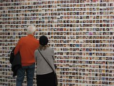 two people standing in front of a wall covered with pictures