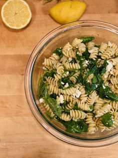 a glass bowl filled with pasta and spinach on top of a wooden cutting board