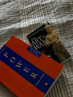 two books sitting on top of a bed next to an orange book case with the word power