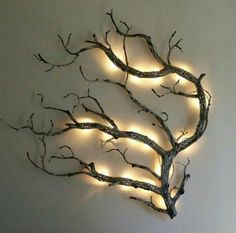 a wall sculpture with lights on it and a tree branch hanging from the side, in front of a white wall