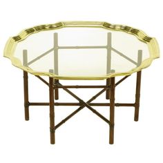 a round glass table with bamboo legs and gold trimmings on the top, against a white background