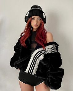 a woman with long red hair wearing headphones and a black jacket is standing in front of a white wall