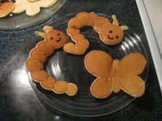 two plates with pancakes shaped like animals on them, and one has a cookie in the shape of a caterpillar