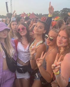 a group of young women standing next to each other at a music festival with their fingers up in the air