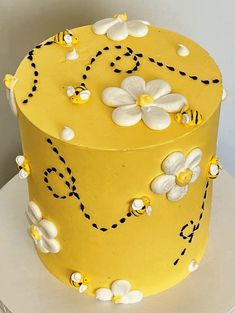 a yellow cake with white flowers and black dots on the top is sitting on a table