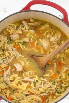 a red pot filled with chicken noodle soup and a wooden spoon in the bowl