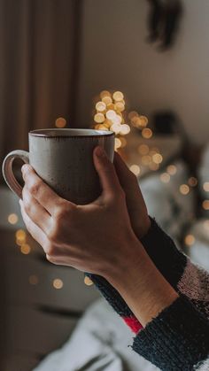 a person holding a coffee cup in front of a christmas tree with lights on it