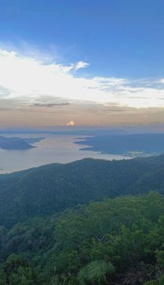 the sun is setting over some trees and water on top of a hill with mountains in the background