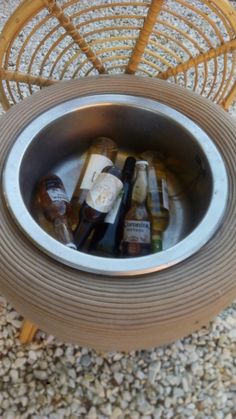 a metal bowl filled with liquor bottles on top of a floor next to a wicker chair