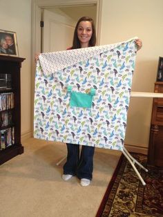 a woman holding up a quilt in front of a bookcase with pictures on it